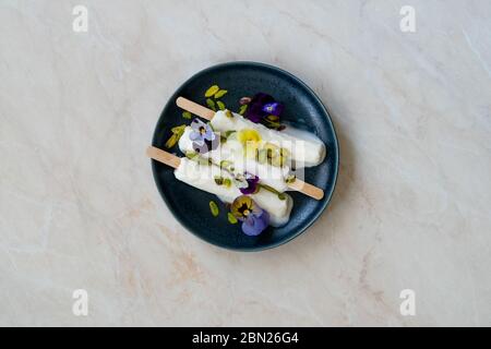 Hausgemachte indische Rajasthani Kulfi Eiscreme mit Stick / Kesariya mit Pistazien und essbare Blumen. Traditionelles Dessert. Stockfoto