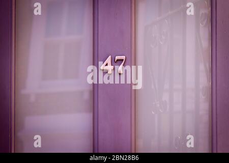 Haus Nummer 47 auf einer hellvioletten Holztür mit großen Glasfenstern, die ein Haus gegenüber reflektieren Stockfoto