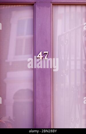 Haus Nummer 47 auf einer hellvioletten Holztür mit großen Glasfenstern, die ein Haus gegenüber reflektieren Stockfoto