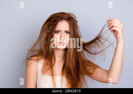 Nahaufnahme Porträt von frustrierten jungen Mädchen mit vermessenen Haaren auf reinem Hintergrund, trägt weiße beiläufige Singlet, hält ihr Haar Stockfoto