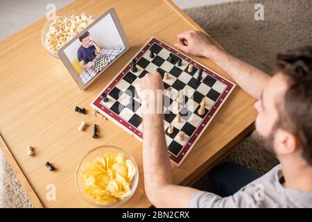 Oben Ansicht des jungen Mannes, der am Couchtisch sitzt und Schachspiel gegen Gegner online in der Heimatisolation spielt Stockfoto