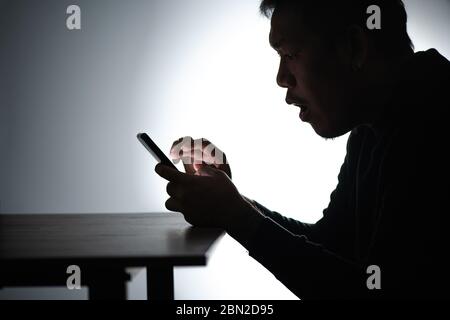Silhouette asiatische Mann arbeitet auf Smartphone. Bärtiger Mann arbeitet von zu Hause aus am Handy. Freelancer man Blogger Arbeiten Sie von zu Hause aus mit dem Handy Stockfoto