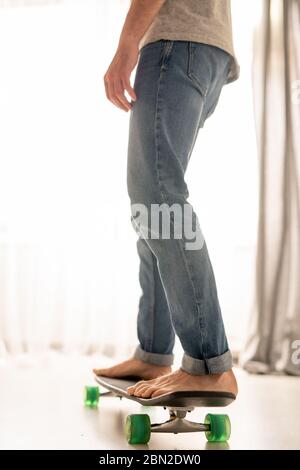 Unkenntlich Mann in Jeans lernen Skateboard über Wohnzimmer in häuslicher Isolation Stockfoto