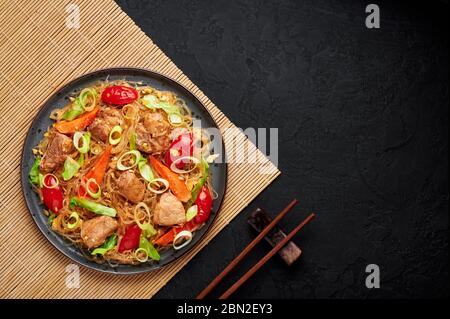 Pad Woon Sen oder Thai Pork Glass Noodle Stir-Fry in schwarzer Platte auf dunklem Schieferhintergrund. Pad Woon Sen ist ein thailändisches Gericht aus Glasbohnennudeln, Fleisch Stockfoto