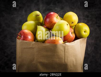 Äpfel und Birnen in einem Papiertütchen Bastelpapier auf dunklem Hintergrund Stockfoto