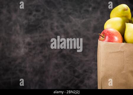 Äpfel und Birnen in einem Papiertütchen Bastelpapier auf dunklem Hintergrund Stockfoto