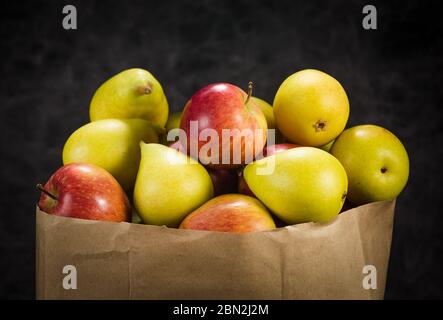Äpfel und Birnen in einem Papiertütchen Bastelpapier auf dunklem Hintergrund Stockfoto