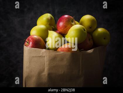 Äpfel und Birnen in einem Papiertütchen Bastelpapier auf dunklem Hintergrund Stockfoto