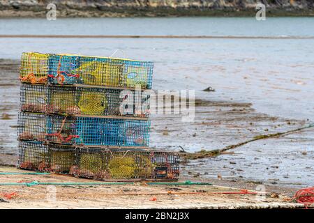 Ein Haufen Hummerfallen auf einem kleinen Holzkahn an einem Strand bei Ebbe. Es gibt neun Fallen in den Stapel, sie haben Steine im Inneren für Gewicht. Stockfoto