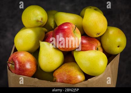 Äpfel und Birnen in einem Papiertütchen Bastelpapier auf dunklem Hintergrund Stockfoto