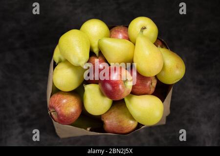 Äpfel und Birnen in einem Papiertütchen Bastelpapier auf dunklem Hintergrund Stockfoto