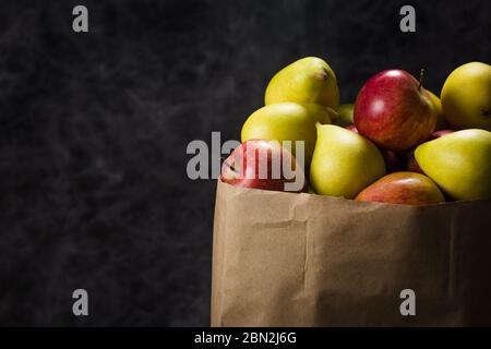 Äpfel und Birnen in einem Papiertütchen Bastelpapier auf dunklem Hintergrund Stockfoto