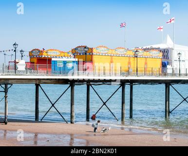 Eine Frau geht mit ihrem Hund unter dem geschlossenen Pier am Strand von Paignton während der Sperrung des Coronavirus, Großbritannien Stockfoto