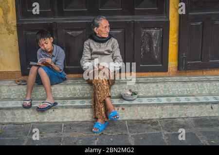 Wundervolle Aussicht auf die alte Straße. Vietnamesen sitzen in der Nähe des Hauses. Hoi an (Hoi an), Vietnam - 12. März 2020. Stockfoto