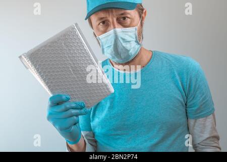 Lieferung Mann posiert mit Paket in Schutzkleidung tragen Baseball-Kappe, Schutzmaske und Handschuhe während Virusinfektion Pandemie outbre Stockfoto