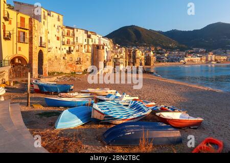 Boote am Strand und sonnige Häuser in Küstenstadt Cefalu bei Sonnenuntergang, Sizilien, Italien Stockfoto