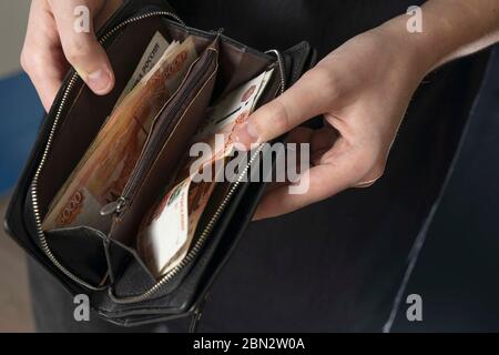 Ein Mann mit einer schwarzen Brieftasche voller russisches Geld. In einer schwarzen Brieftasche, Banknoten sind meist 5,000 Rubel pro Stück. Gehalt und Rente erhöht, Leistungen Stockfoto