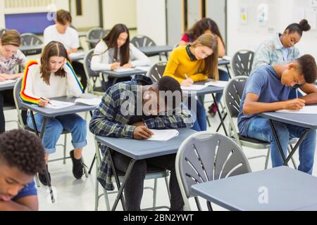 Fokussierte Schüler, die an den Schreibtischen im Klassenzimmer die Prüfung ablegen Stockfoto