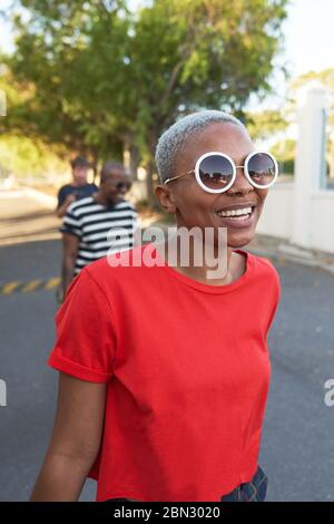 Glückliche junge Frau in Sonnenbrille zu Fuß in der Straße Stockfoto