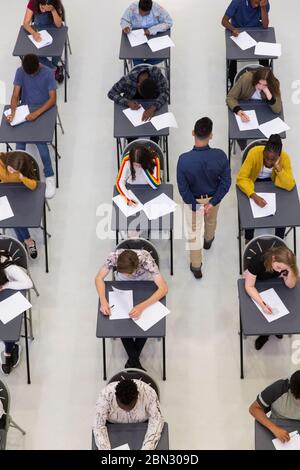 Lehrer überwacht High School Studenten, die Prüfung an Schreibtischen Stockfoto