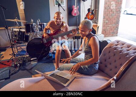 Lächelnde Musiker mit Laptop und Gitarre im Aufnahmestudio Stockfoto