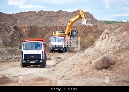 GRODNO, WEISSRUSSLAND - MAI 2020: Zwei Mehrtonne-MAZ-LKW im Prozess der Verladung von Erz durch Hyundai-Bagger für den Export von Mineralien aus dem Tagebau m Stockfoto