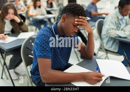 Fokussierter High School Junge, der Prüfung am Schreibtisch im Klassenzimmer nimmt Stockfoto