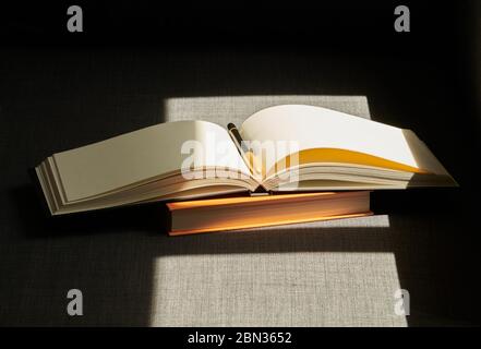 Ein Buch und ein Notizbuch mit einem Stift in einem vollen Sonnenschein auf dem grauen Sofa Stockfoto