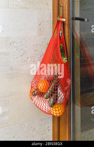 Lebensmittelzustellung oder Spende in einem Netzbeutel am Türgriff während der Quarantäne. Kontaktlose Lebensmittelzustellung vom Supermarkt nach Hause. Sicheres Einkaufen Stockfoto