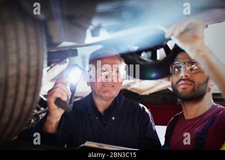 Männliche Mechaniker mit Taschenlampe arbeitet unter Auto in der Auto-Werkstatt Stockfoto