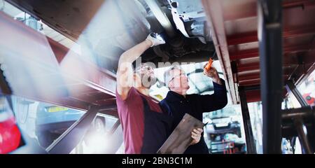 Männliche Mechaniker mit Taschenlampen arbeiten unter Auto in der Autowerkstatt Stockfoto