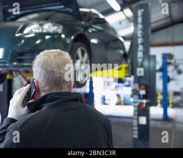 Männliche Mechaniker sprechen auf Smartphone in Auto-Werkstatt Stockfoto