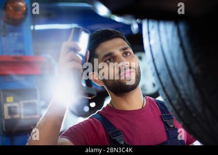 Fokussierte männliche Mechaniker mit Taschenlampe Prüfung Reifen in der Auto-Werkstatt Stockfoto