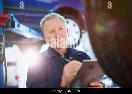 Lächelnder Mechaniker mit Klemmbrett, der in der Autowerkstatt arbeitet Stockfoto