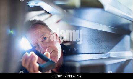 Männliche Mechaniker mit Taschenlampe arbeitet unter Auto Stockfoto