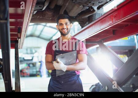 Portrait zuversichtlich, männliche Mechaniker mit Klemmbrett arbeitet unter dem Auto in der Autowerkstatt Stockfoto