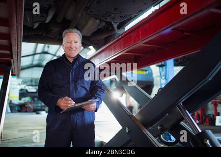 Portrait selbstbewusst, lächelnd Mechaniker mit Klemmbrett arbeiten unter Auto in der Autowerkstatt Stockfoto