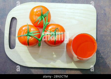 Tomatensaft unter frischen Tomaten auf der obersten Ansicht Küche Holzbrett. Stockfoto