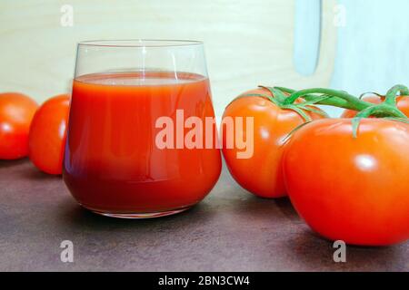 Tomatensaft unter frischen Tomaten auf der obersten Ansicht Küche Holzbrett. Stockfoto