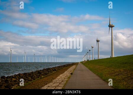 Weg durch den Deich zum riesigen Windmühlenpark mit riesigen Turbinen in den Niederlanden Noordoostpolder, Grünstrom-Windmühlenpark in Flevoland Stockfoto