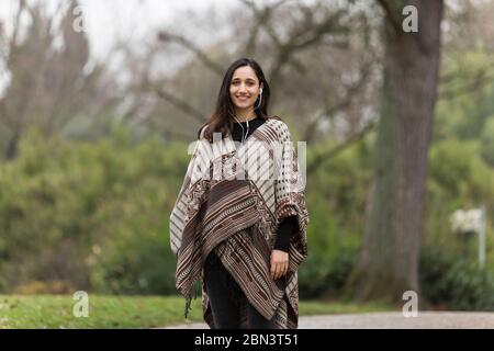 Schöne indische Frau trägt Poncho und lächelt weit im Park. Stockfoto