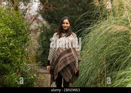 Junge Frau mit Poncho zwischen hohen Gras im Herbst stehen. Stockfoto