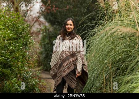Junge Frau mit Poncho posiert zwischen hohen Gras im Herbst. Stockfoto