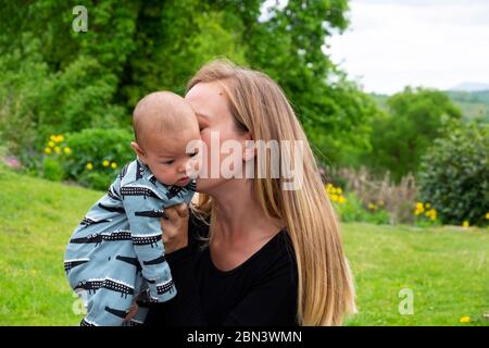 Junge Mutter während Pandemie halten Alarm Baby Junge küssen und Kuscheln draußen zu Hause im Garten bleiben Mai 2020 Wales GROSSBRITANNIEN KATHY DEWITT Stockfoto