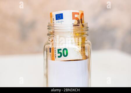 Komposition mit Spargeld-Banknoten (50 EURO) in einem Glas mit leerem weißen Etikett oder Notiz für Ihren Text. Konzept der Investition und des Halts von Geld, Stockfoto