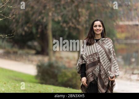 Junge Frau aus dem Nahen Osten trägt Poncho und lächelt im Park. Stockfoto