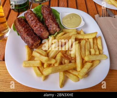 Ein klassisches, traditionelles rumänisches Gericht aus gemischtem Hackfleisch namens 'Mici', serviert auf einem Teller mit Pommes und Senf, ein rumänisches Gericht zum Mitnehmen während Sum Stockfoto