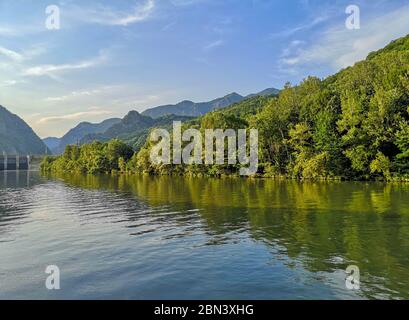 Fluss fließt friedlich mit grünen Bäumen am Ufer und Berglandschaft im fernen Hintergrund, eine ruhige Szene irgendwo in Rumänien Stockfoto