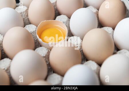 Hühnereier in Bio-Verpackung Nahaufnahme. Ei halb gebrochen unter anderen Eiern. Food-Fotografie Stockfoto