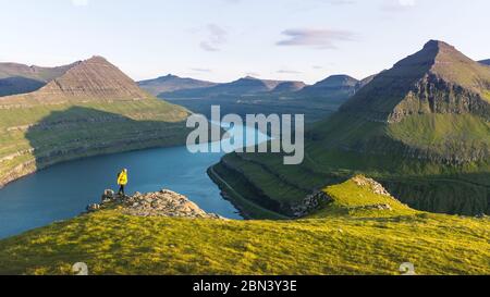 Einsamer Tourist in gelber Jacke mit Blick auf majestätische Fjorde von Funningur, Insel Eysturoy, Färöer. Landschaftsfotografie Stockfoto